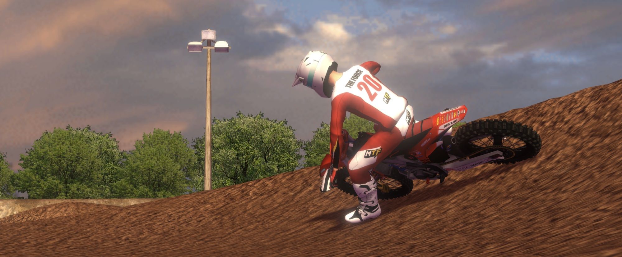 Rider in red gear riding a red bike up a dirt berm at sunset